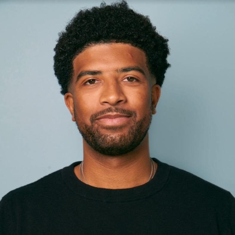 K.J. Smith in a black crewneck against a pale blue backdrop