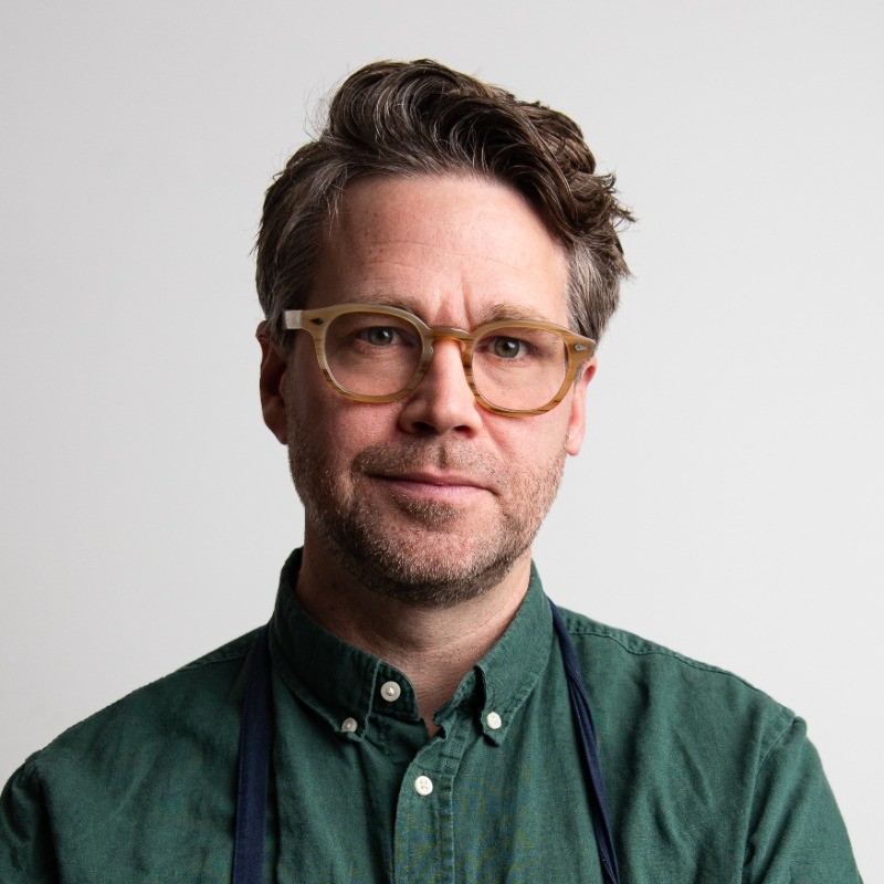 Marcus Jernmark in a green chef&rsquo;s shirt and navy apron against a pale grey backdrop