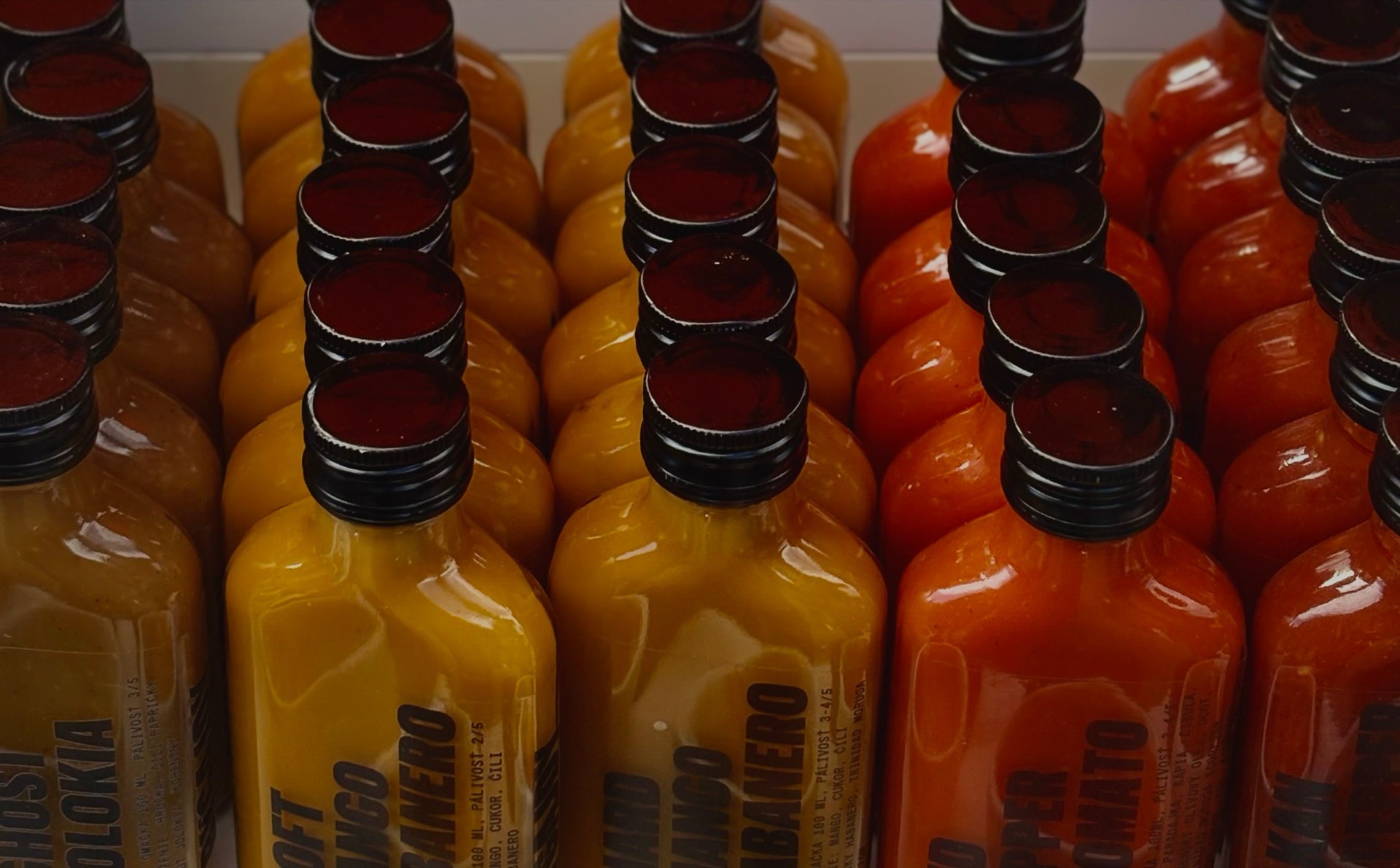Rows of labelled hot sauce bottles in green, yellow, and red, packed upright in a case